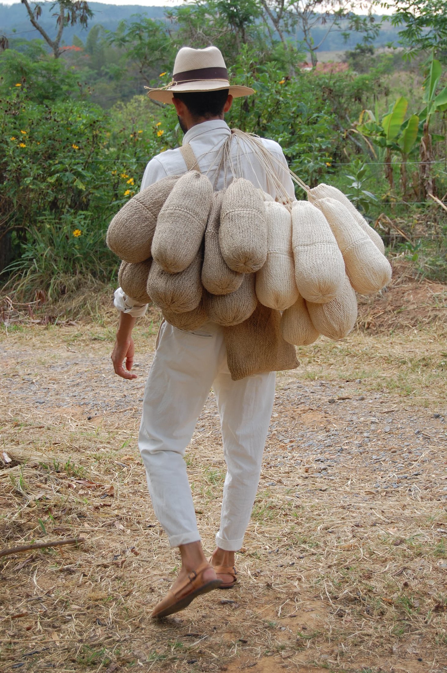 Albeiro camina por un sendero del campo cargando al hombro sus mochilas de fique, rumbo a una exposición